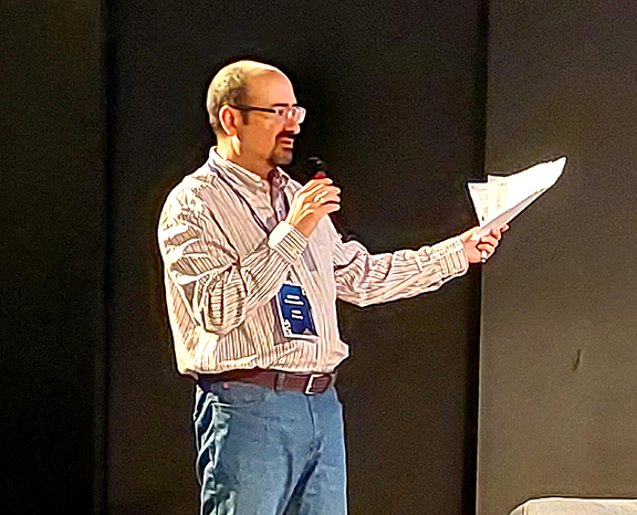 A man standing, talking to microphone and holding a paper
