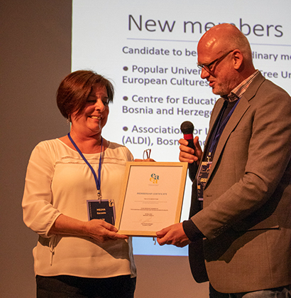 A woman and a man holding a framed certificate, man holding microphone