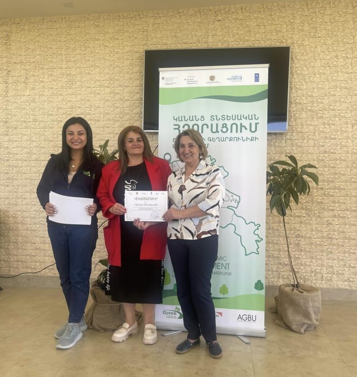 Women holding certificates in front of a banner.