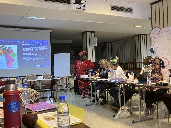 A woman standing in front of a screen that says "Welcome to Africa, the land of wealth", a group of learners is in front of her