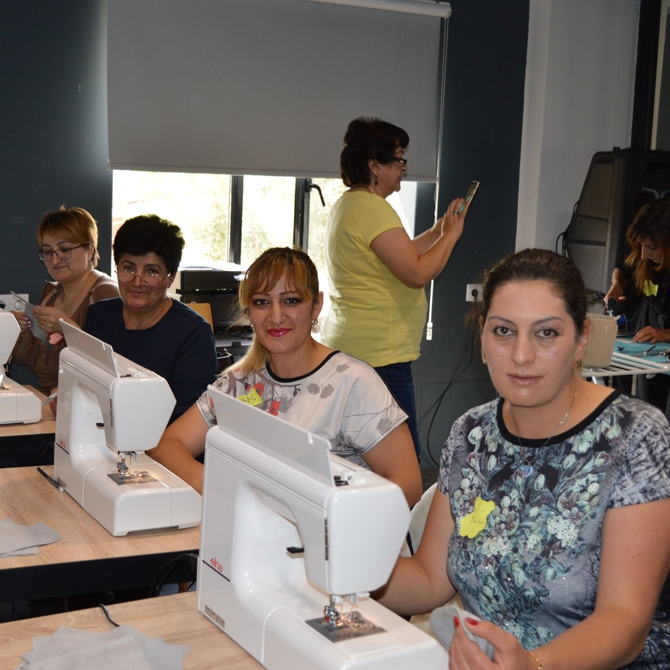 Women sitting in front of sewing machines and posing for the photo.