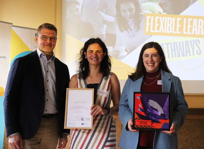 three people pictured. One woman holding a certificate and another an artwork