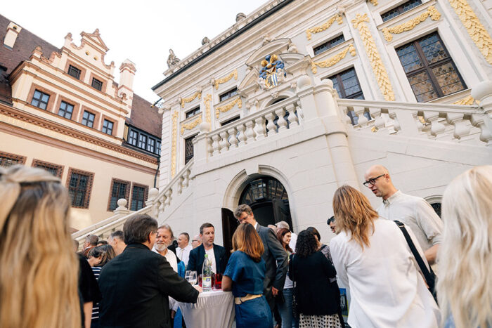 A group of people gathered in front of historical building, having drinks